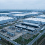 Vue aérienne réaliste d’un vaste data center hyperscale moderne entouré de postes électriques, de transformateurs et de lignes à haute tension, sous une lumière froide.