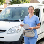Une infirmière libérale souriante se tient près de son véhicule avec une mallette médicale et un dossier d’assurances, dans une ambiance professionnelle et lumineuse.